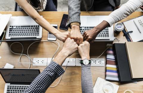 multiple closed hands touching in a circle over laptops